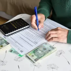 Emeryt wypełnia dokumenty dotyczące zatrudnienia na umowę zlecenie, składki i limity dorabiania. Obok leżą pieniądze i kalkulator.
