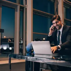 Biznesmen na podróży służbowej rozmawia przez telefon, pracując przy laptopie. Nagle czuje się źle, co może oznaczać zwolnienie L4 i nieprzewidziane koszty.