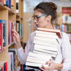 Absolwentka kierunków humanistycznych, która marzy o stażu w archiwum lub bibliotece, wybiera książki z regału.