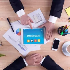 Rekrutacja ukryta: jak znaleźć oferty bez nazwy firmy? Na tablecie widnieje napis "RECRUITMENT", obok dokumenty i akcesoria biurowe.