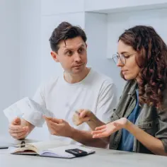 Para rozmawia o dokumentach i rachunkach przy stole z laptopem i notatnikiem.
