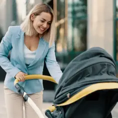 Uśmiechnięta kobieta w eleganckim stroju, z wózkiem dziecięcym, symbolizuje szukanie pracy dla matki po długim urlopie macierzyńskim i powrót na rynek.