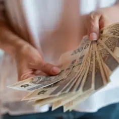 Dłonie trzymające plik banknotów 200 zł. Dowiedz się, jak prawidłowo policzyć ciągłość zatrudnienia do nagrody jubileuszowej.