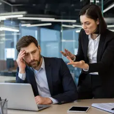 Zestresowany mężczyzna przy laptopie, kobieta gestykuluje. Jak udowodnić zatrudnienie bez umowy przed sądem pracy?