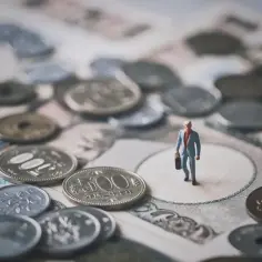 Mała figurka biznesmena na japońskich banknotach i monetach. Symbolizuje podróż pracownika tymczasowego z agencji, który oczekuje na dietę delegacyjną.