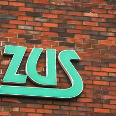 Zielone litery ZUS na ceglanej ścianie.