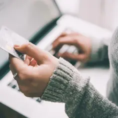 Karta kredytowa firmowa w ręku, laptop w tle. Rozliczenie prywatnych wydatków w trakcie delegacji.