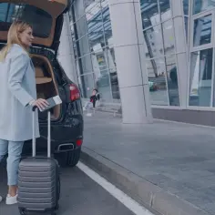Kobieta z walizką i paszportem przy samochodze. Dojazd z lotniska do hotelu jako czas pracy, zasady z orzecznictwa sądu.