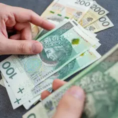 Ręce liczą polskie banknoty 100 zł. Zatrudnienie emeryta mundurowego może oznaczać zbieg tytułów do ubezpieczeń społecznych.